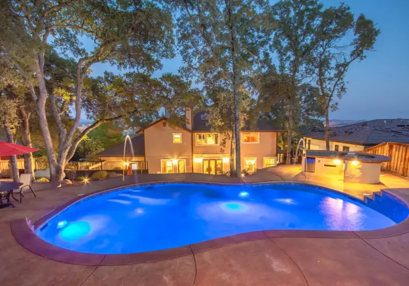 A large pool with lights on in the back yard.