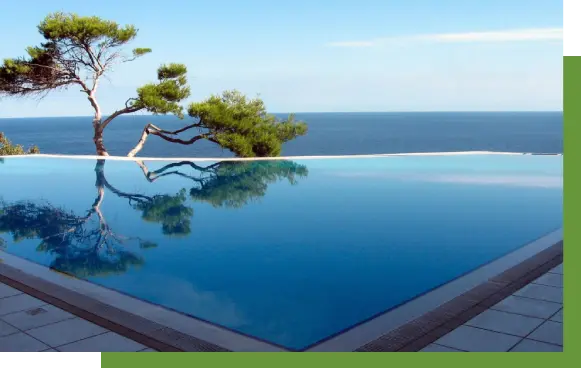 A pool with a view of the ocean and trees.